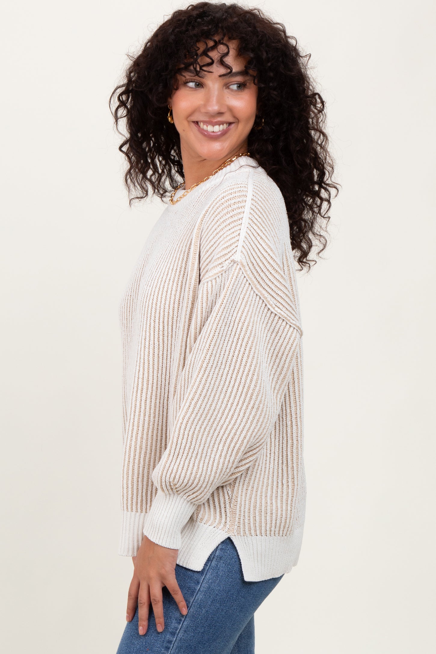 woman wearing a soft cream striped oversized sweater with long sleeves and a relaxed fit, smiling to the side