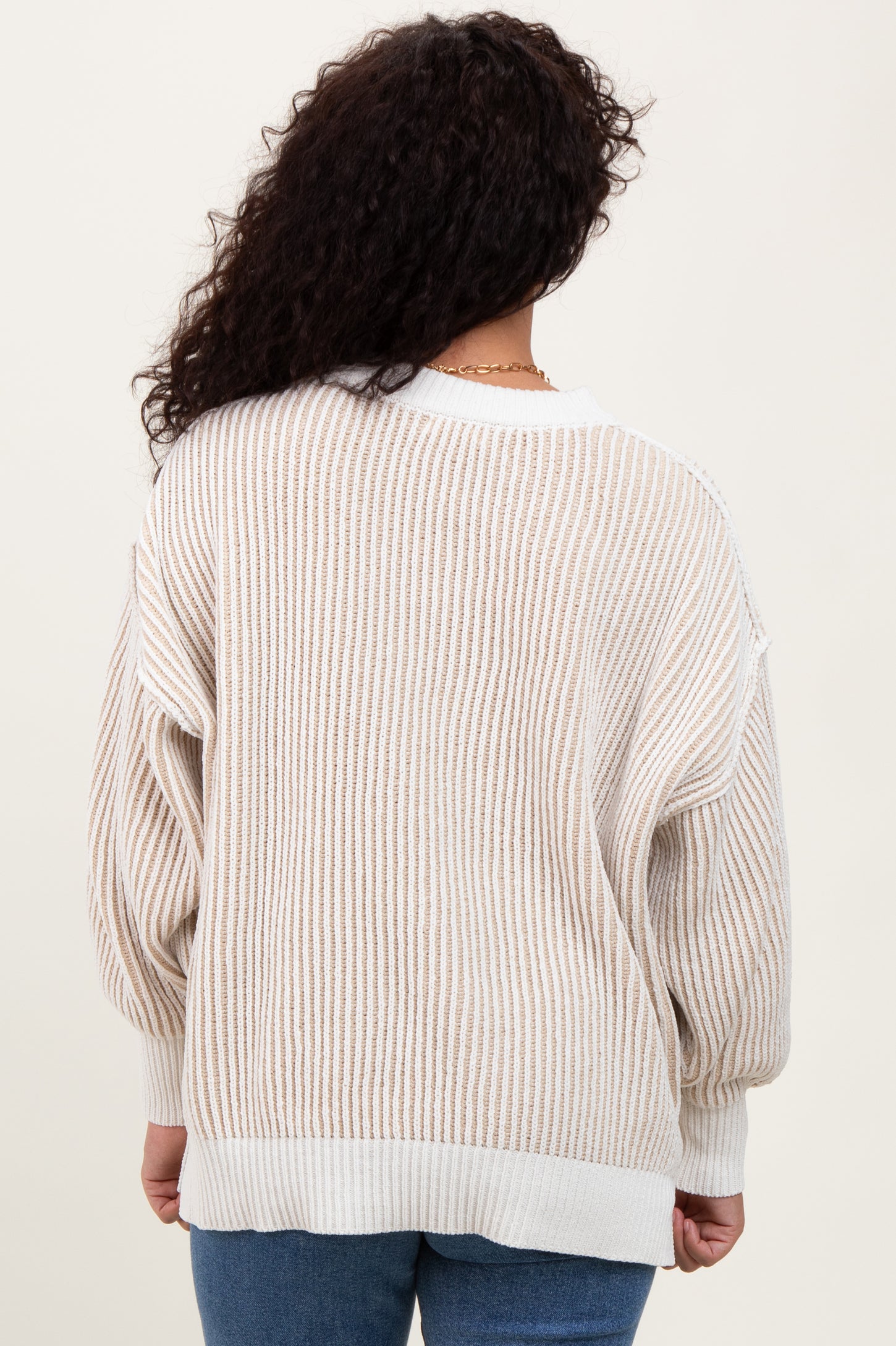 woman wearing a beige and cream striped oversized sweater, showing the back view and relaxed fit