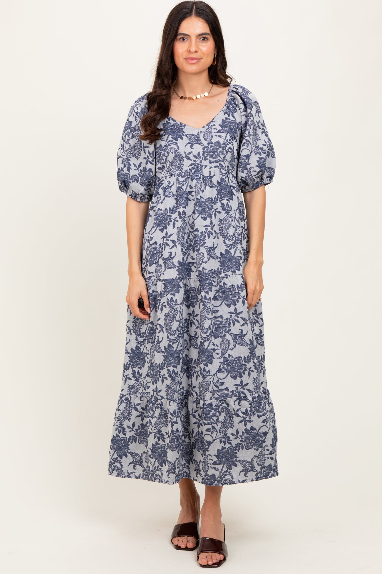 woman wearing a navy blue floral maxi dress with puff sleeves and a v-neckline, standing and smiling
