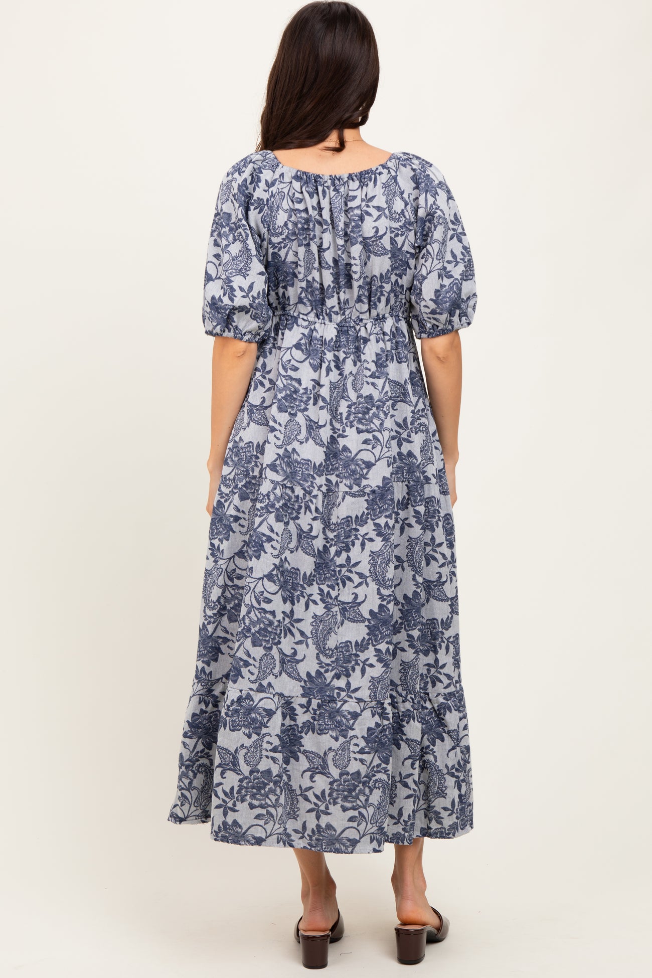 woman wearing a navy blue floral maxi dress with puff sleeves and a cinched waist, viewed from the back