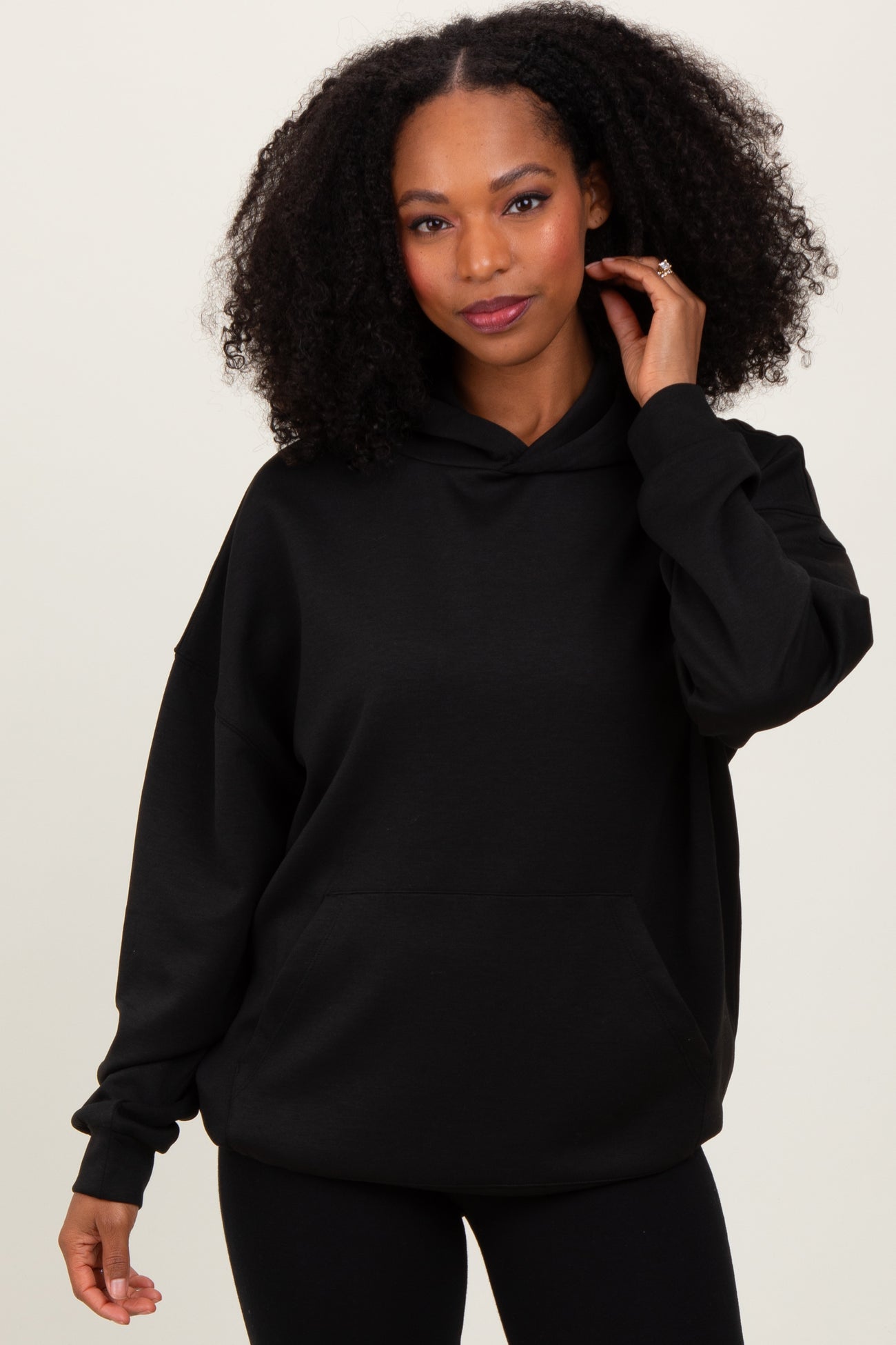 woman wearing a black oversized hoodie with a front pocket and a hood, styled with black leggings