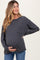 woman wearing a charcoal gray long sleeve maternity top, showing her baby bump while posing with one hand on her belly