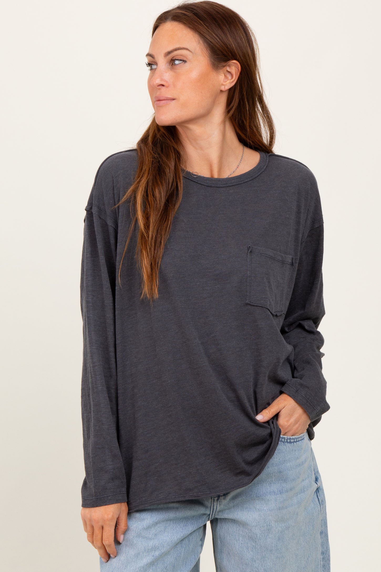 woman wearing a dark gray long sleeve t-shirt with a pocket and relaxed fit, styled with light blue jeans