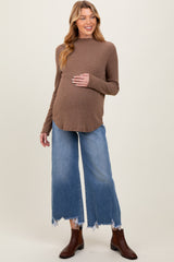 woman wearing a brown maternity sweater and blue wide-leg jeans, showing her baby bump
