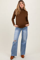 woman wearing a brown long sleeve maternity top and distressed light blue jeans, showing a baby bump