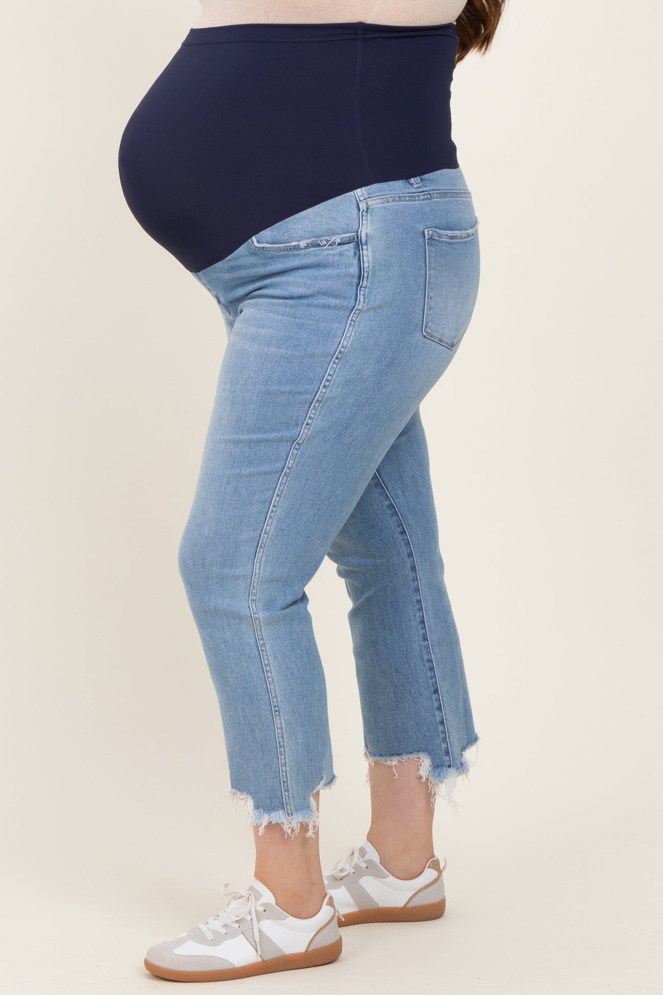 woman wearing light wash maternity jeans with a dark blue belly panel and frayed hem, showing her baby bump
