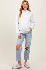 woman wearing a white hooded maternity sweater and blue distressed jeans, showcasing her baby bump