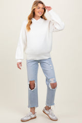 woman wearing a white knit maternity hoodie and distressed light blue jeans, gently touching her baby bump