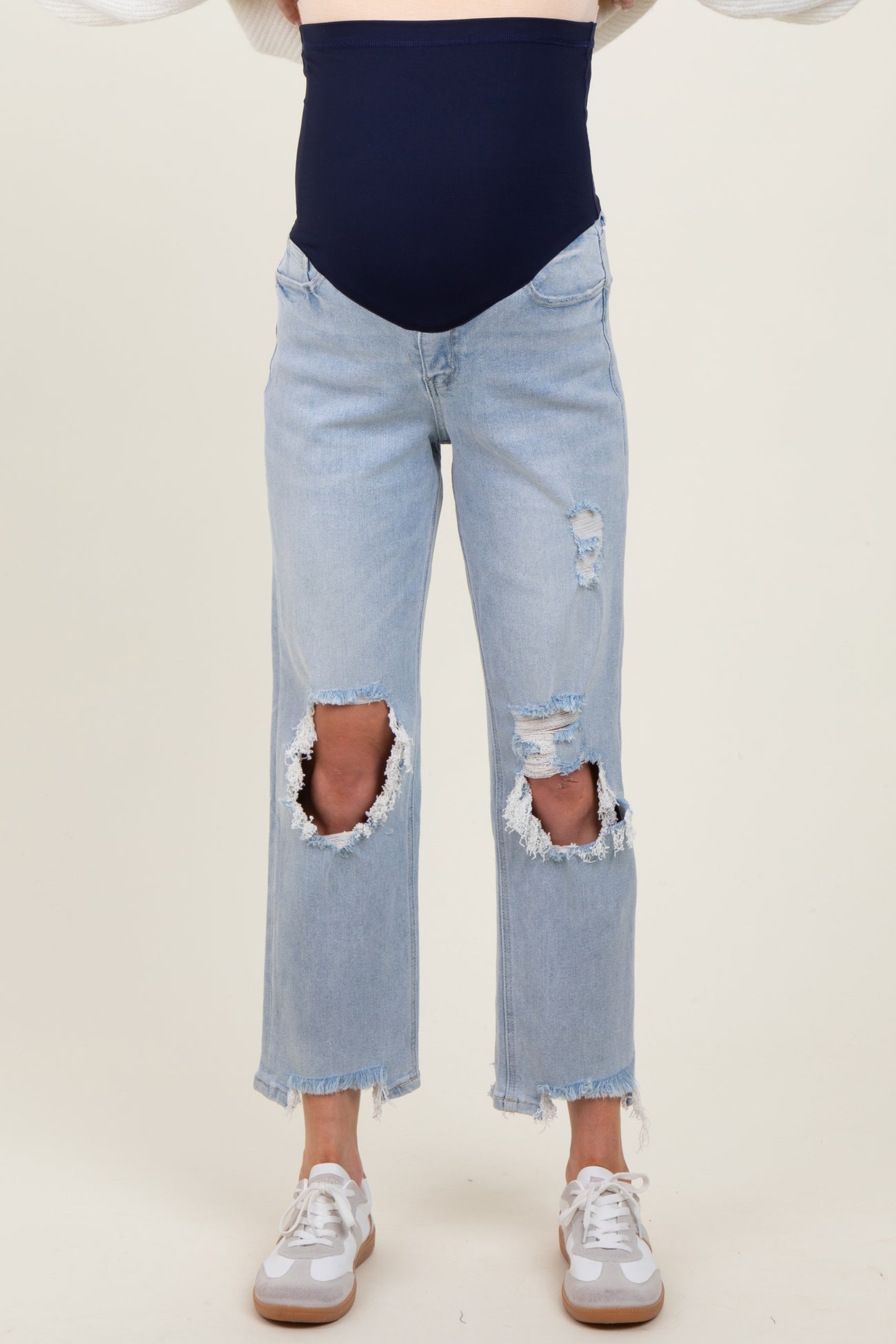 woman wearing light blue distressed maternity jeans with a navy blue over-the-bump band and white sneakers