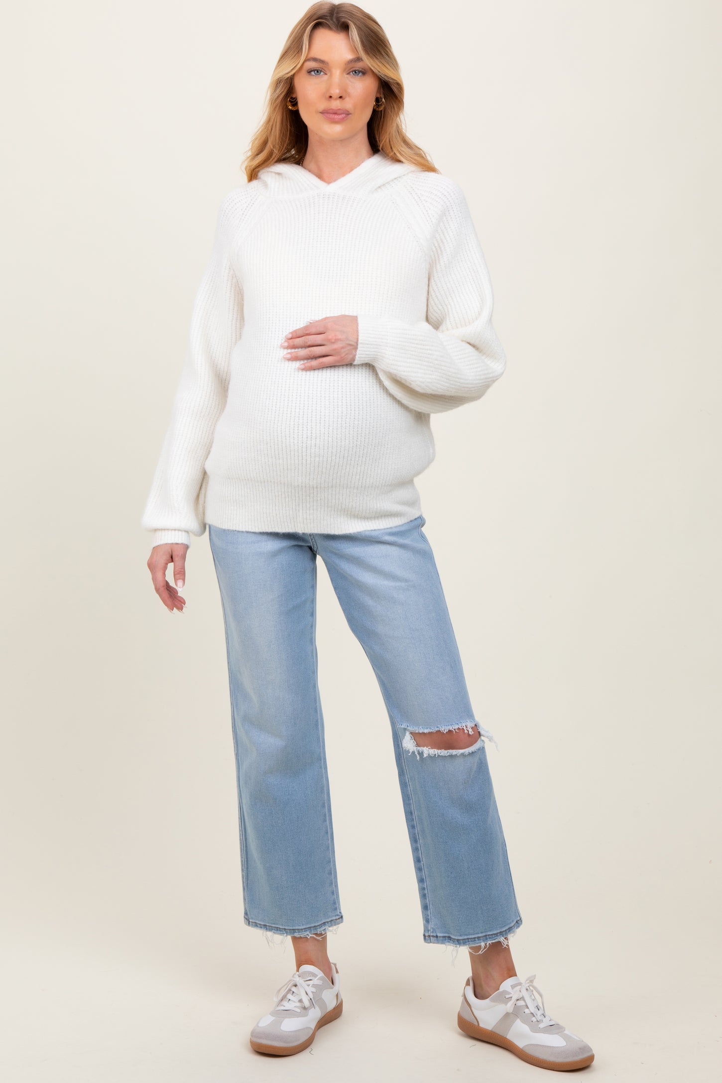 woman wearing a white ribbed maternity hoodie and blue distressed jeans, holding her baby bump