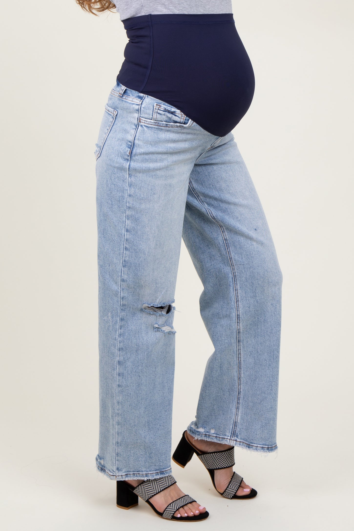 woman wearing light blue distressed maternity jeans with a dark blue over-the-bump waistband and black heeled sandals
