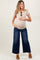 woman wearing a beige short sleeve maternity top and blue wide-leg jeans, holding her baby bump