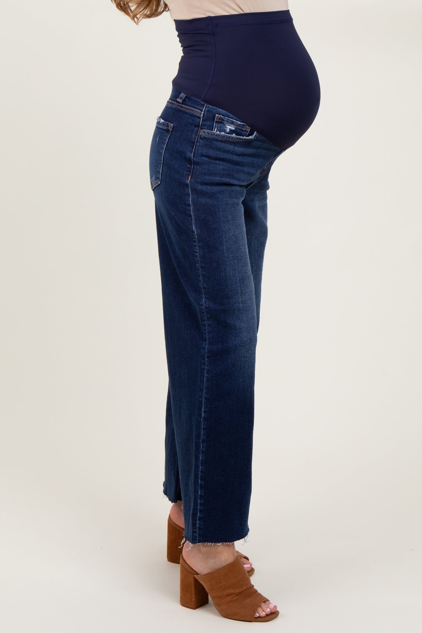 woman wearing dark blue maternity jeans with a supportive belly panel, showcasing her baby bump while standing sideways