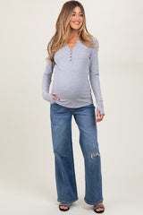 woman wearing a gray long sleeve maternity top with buttons and distressed blue wide-leg jeans, holding her baby bump