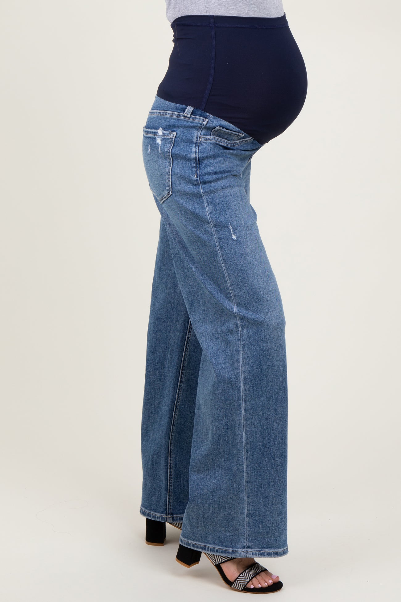 woman wearing distressed blue maternity wide-leg jeans with a navy belly band and showing her baby bump