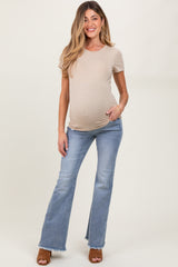 woman wearing a beige short sleeve maternity top and blue flared jeans, showcasing her baby bump