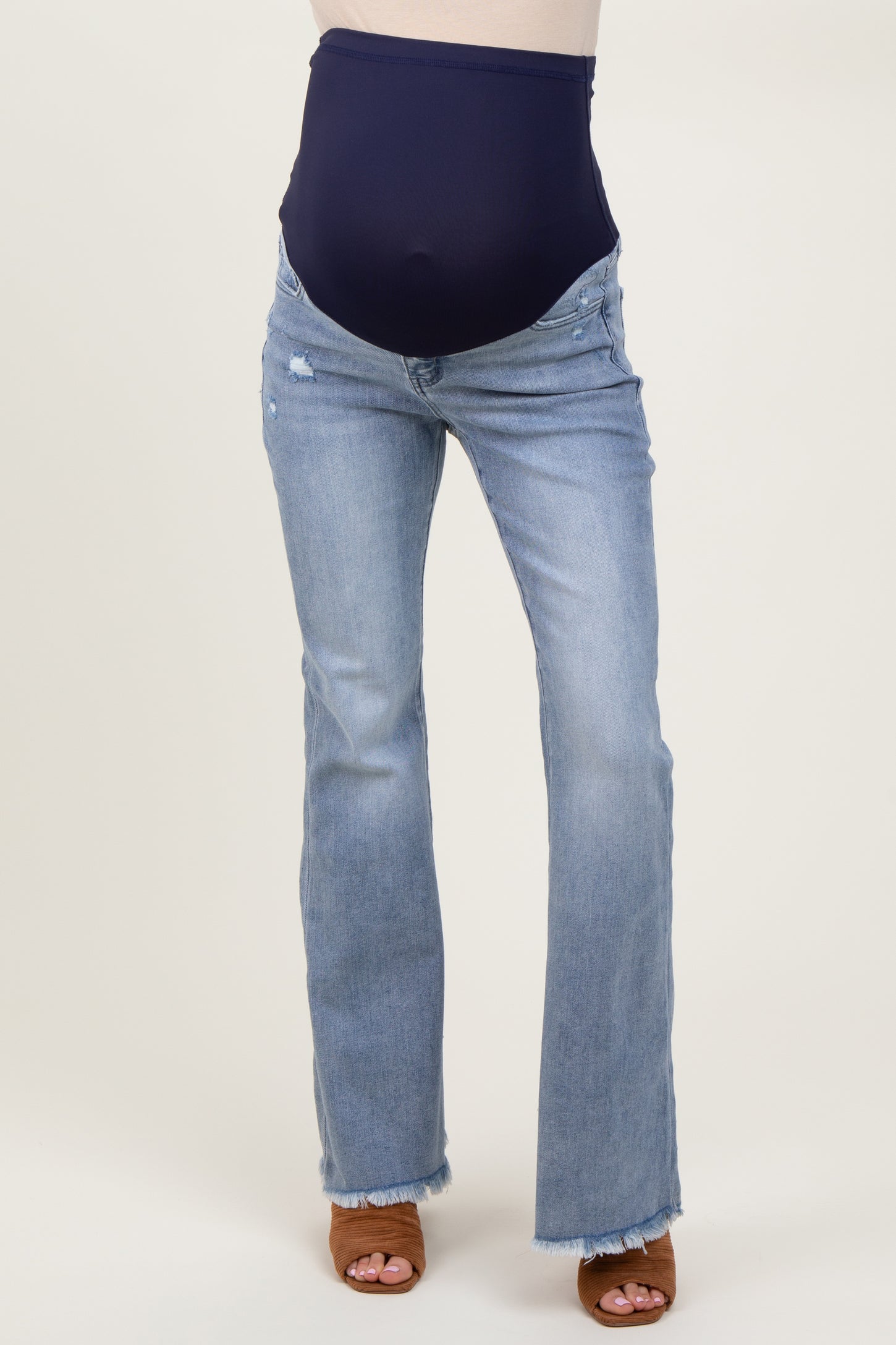 woman wearing maternity light wash flared jeans with a navy blue over-the-bump panel and brown heeled sandals
