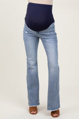 woman wearing maternity light wash flared jeans with a navy blue over-the-bump panel and brown heeled sandals