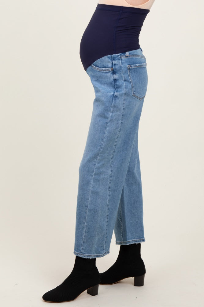 woman wearing light blue maternity jeans with a dark blue belly panel, showing a visible baby bump and styled with black ankle boots