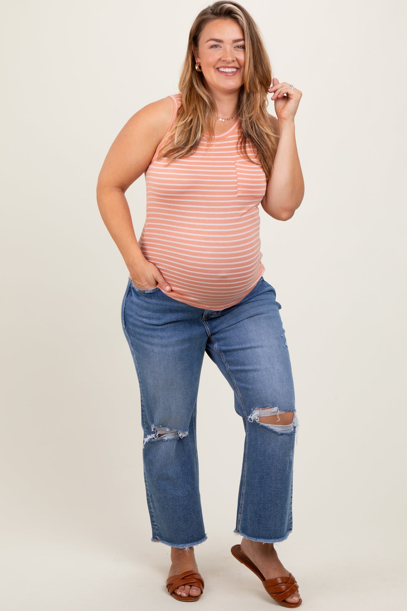 woman wearing a striped maternity tank top and distressed blue jeans, revealing her baby bump