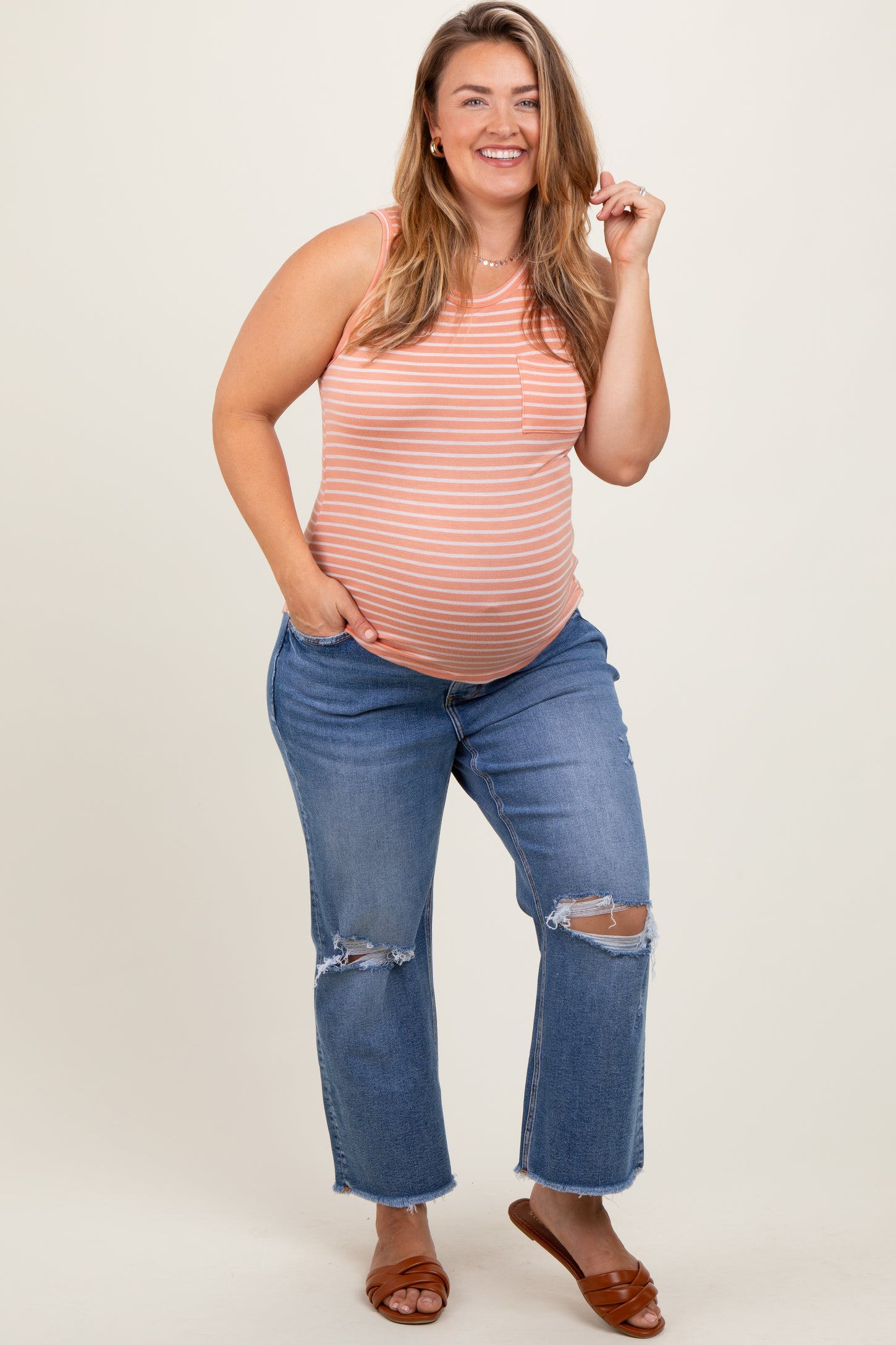 woman wearing a striped maternity tank top and distressed blue jeans, revealing her baby bump
