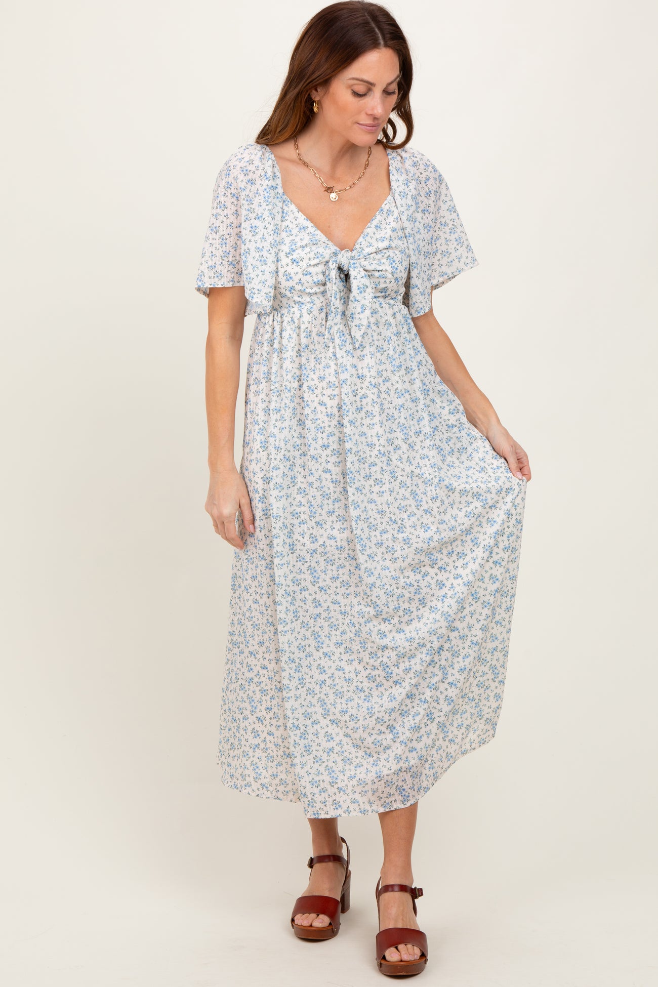 woman wearing a light blue floral maxi dress with short sleeves and a waist tie, standing on a neutral background