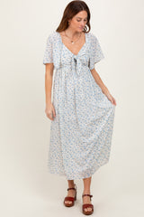 woman wearing a light blue floral maxi dress with short sleeves and a waist tie, standing on a neutral background