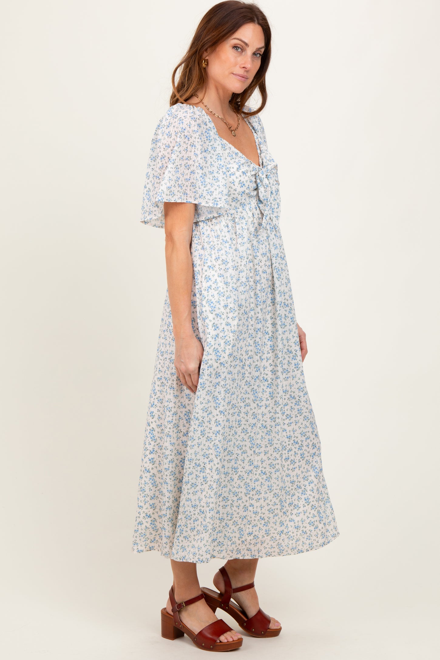 woman wearing a light blue floral maxi dress with short flutter sleeves and a tied neckline