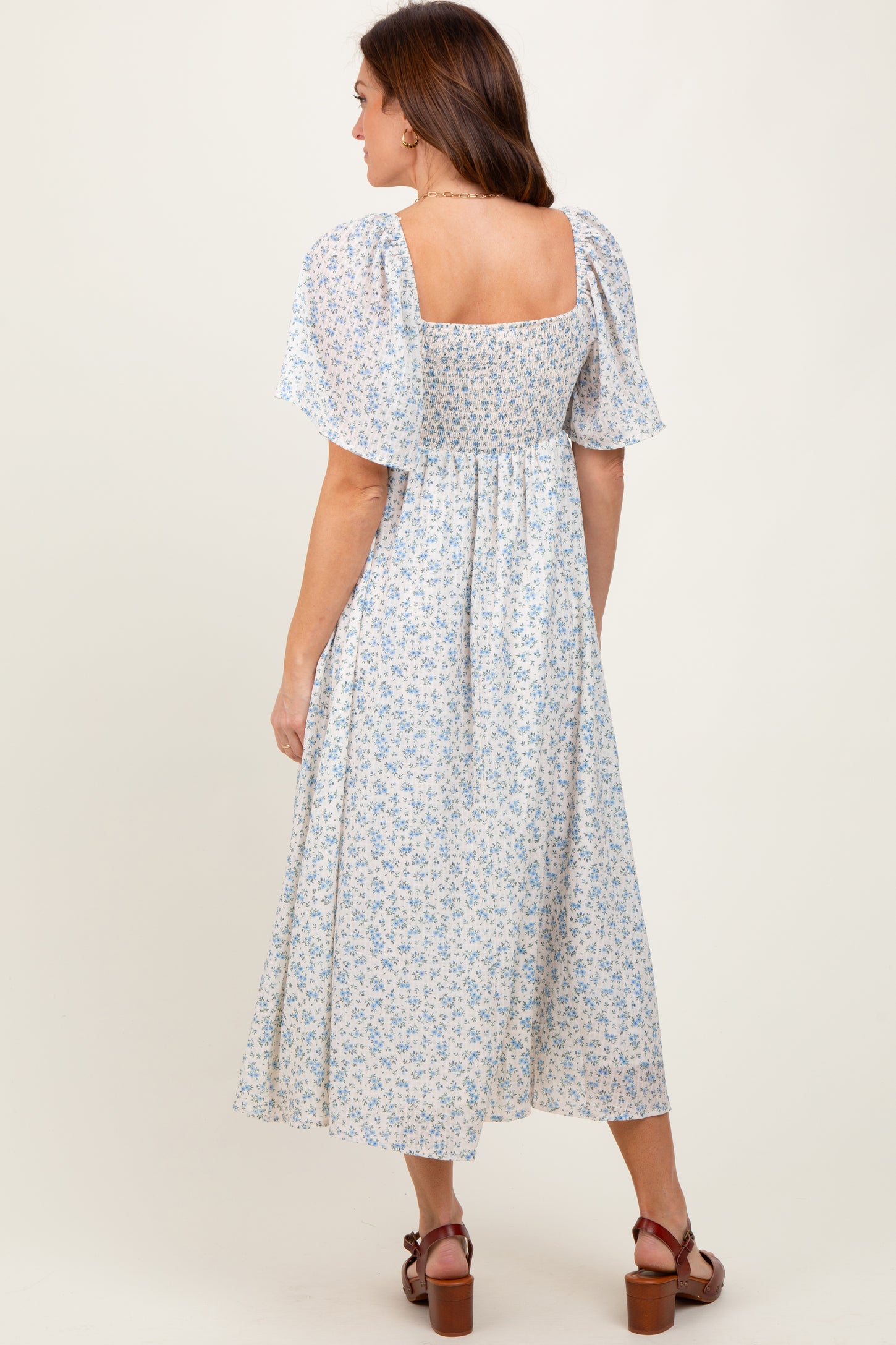 woman wearing a blue and white floral midi dress with a square neckline and flutter sleeves, seen from the back