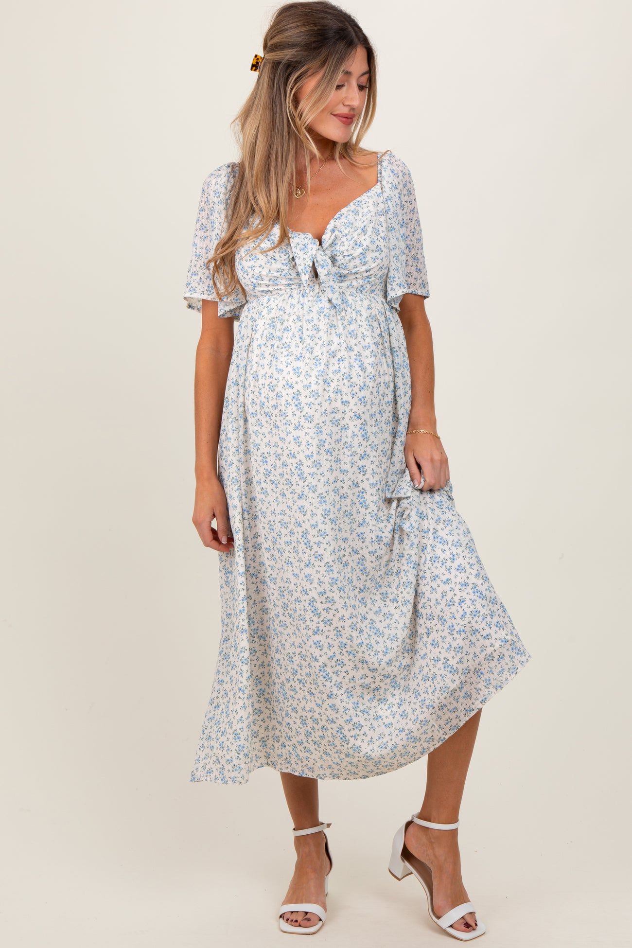 woman wearing a light blue floral maternity dress with short sleeves and a tie front, showing her baby bump