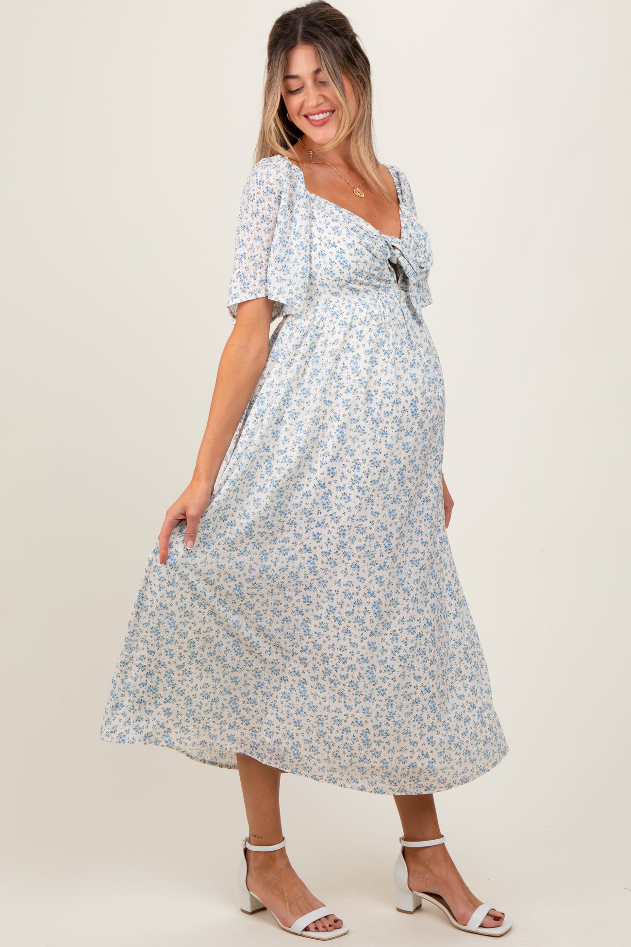 woman wearing a light blue floral maternity maxi dress with puff sleeves and a tie detail, showcasing her baby bump