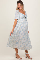 woman wearing a light blue floral maternity maxi dress with puff sleeves and a tie detail, showcasing her baby bump