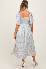 woman wearing a blue and white floral maternity dress with short puff sleeves and a smocked bodice, showing her baby bump