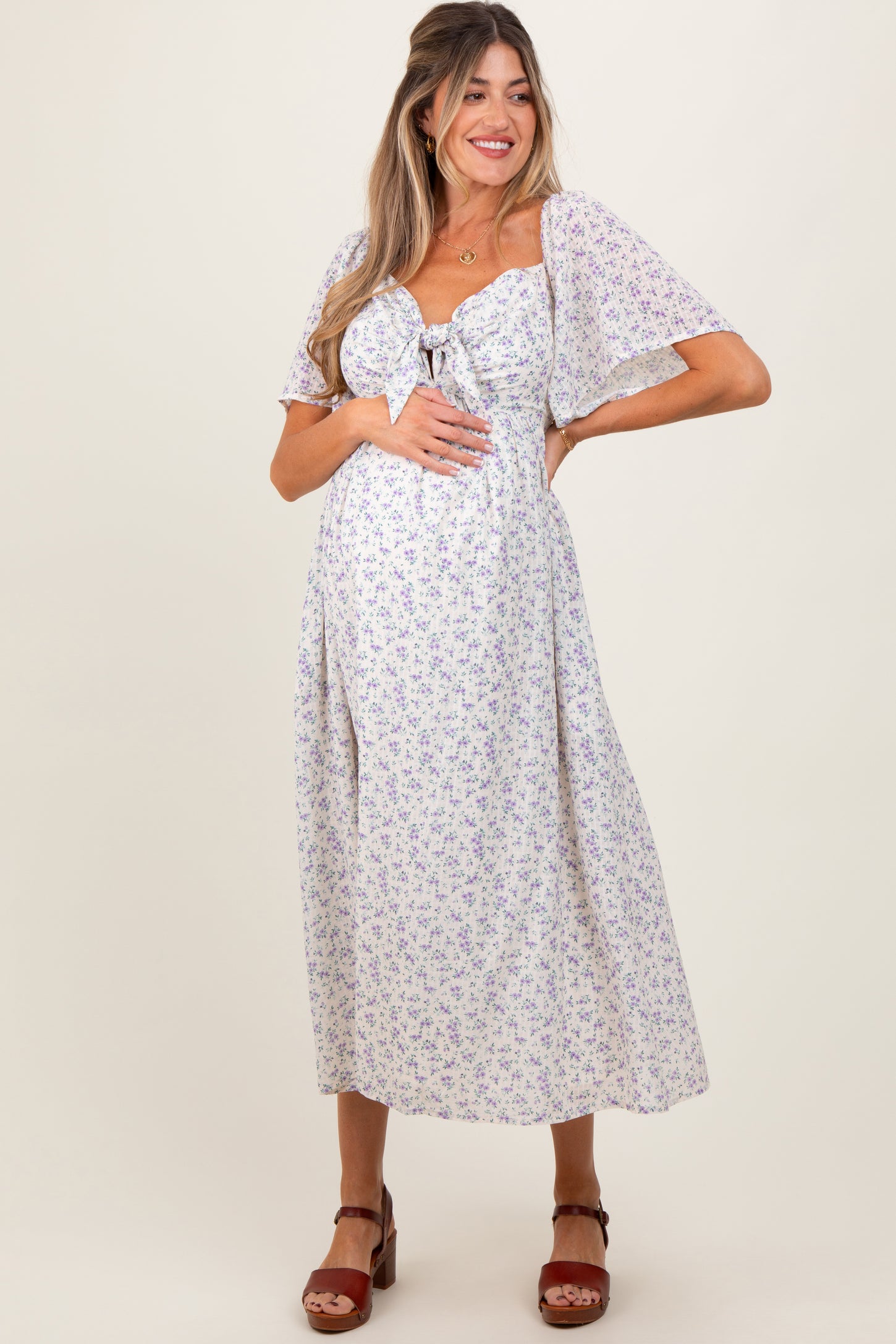 woman wearing a light purple floral maternity dress with short flutter sleeves and a tied front, showing her baby bump
