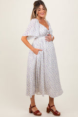 woman wearing a white floral print maternity dress with short flutter sleeves and pockets, holding her baby bump