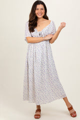 woman wearing a floral print maxi dress with short sleeves and tie detail at the neckline, smiling and posing