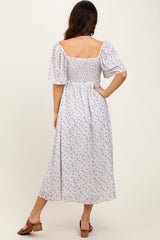 woman wearing a white floral midi dress with short sleeves and a smocked back, standing with her back to the camera