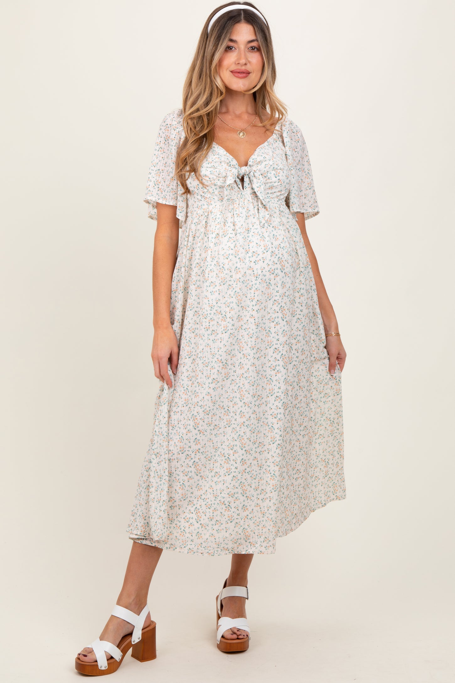 woman wearing a floral print maternity dress with short flutter sleeves and a tie front, showing her baby bump