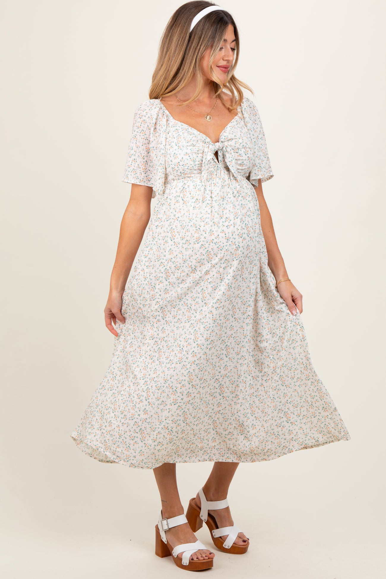 woman wearing a white floral maternity dress with short sleeves and a tie front, showing her baby bump