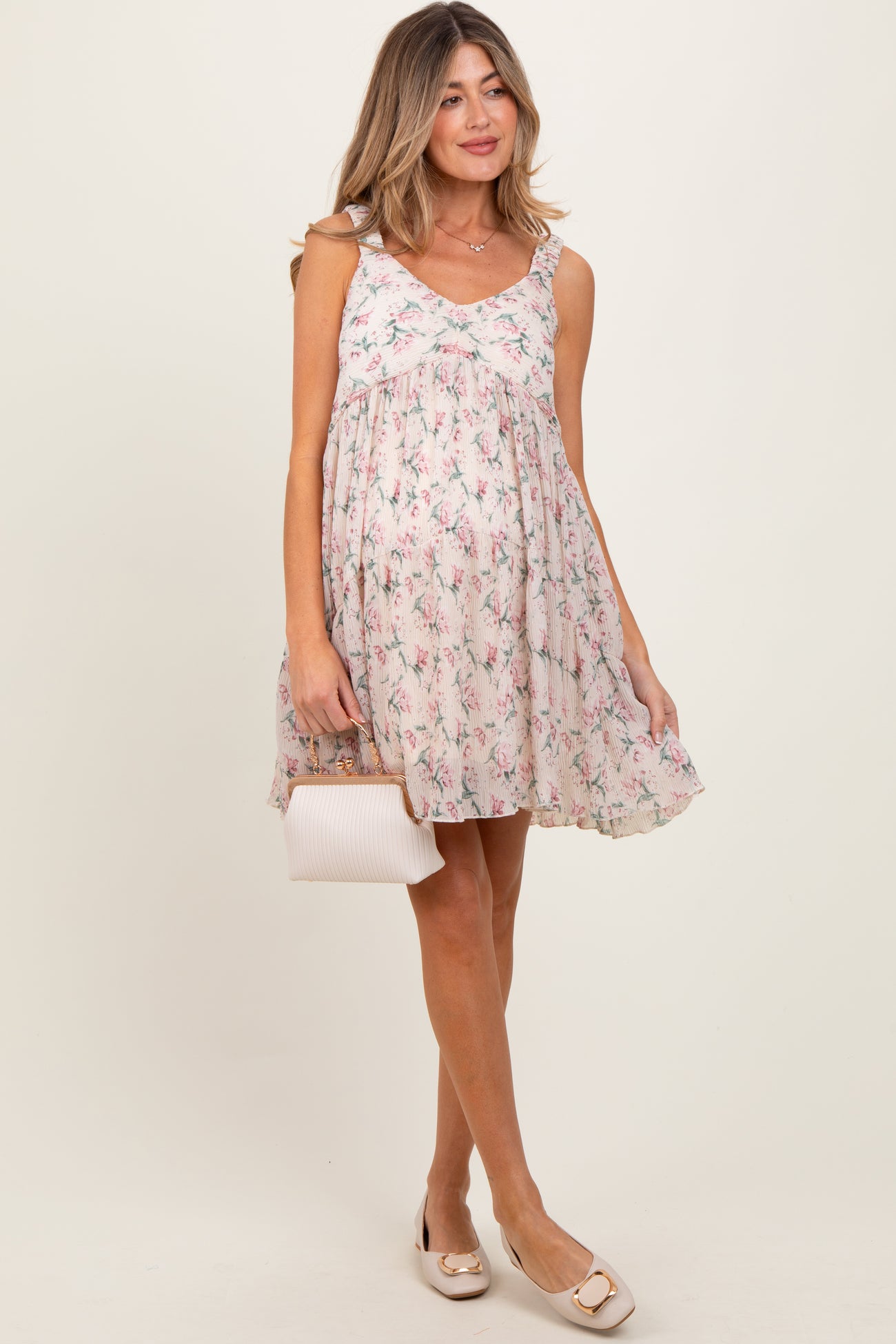 woman wearing a floral print maternity dress with spaghetti straps and a flowy fit, holding a small handbag