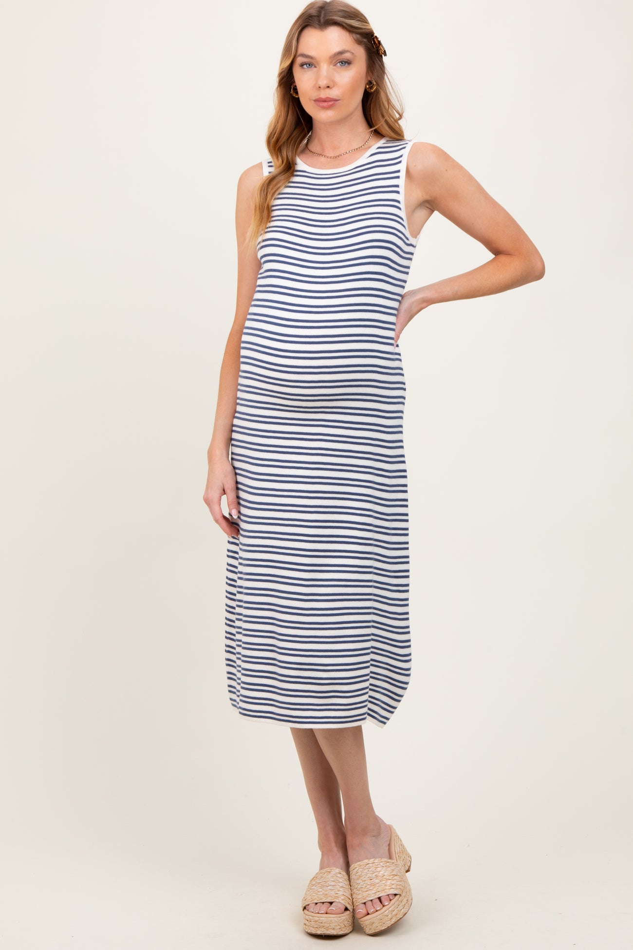 woman wearing a striped maternity dress with a fitted silhouette and side slits, showcasing her baby bump