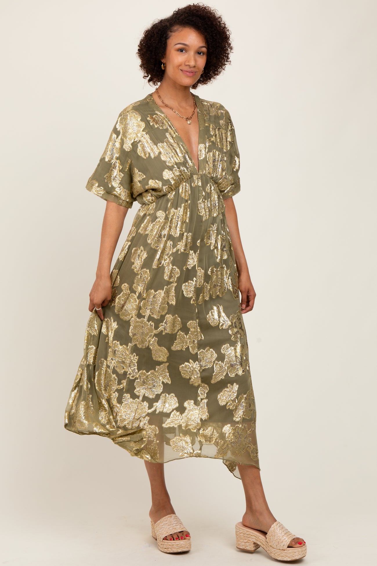 woman wearing an olive green floral maxi dress with metallic gold accents and a deep v-neckline