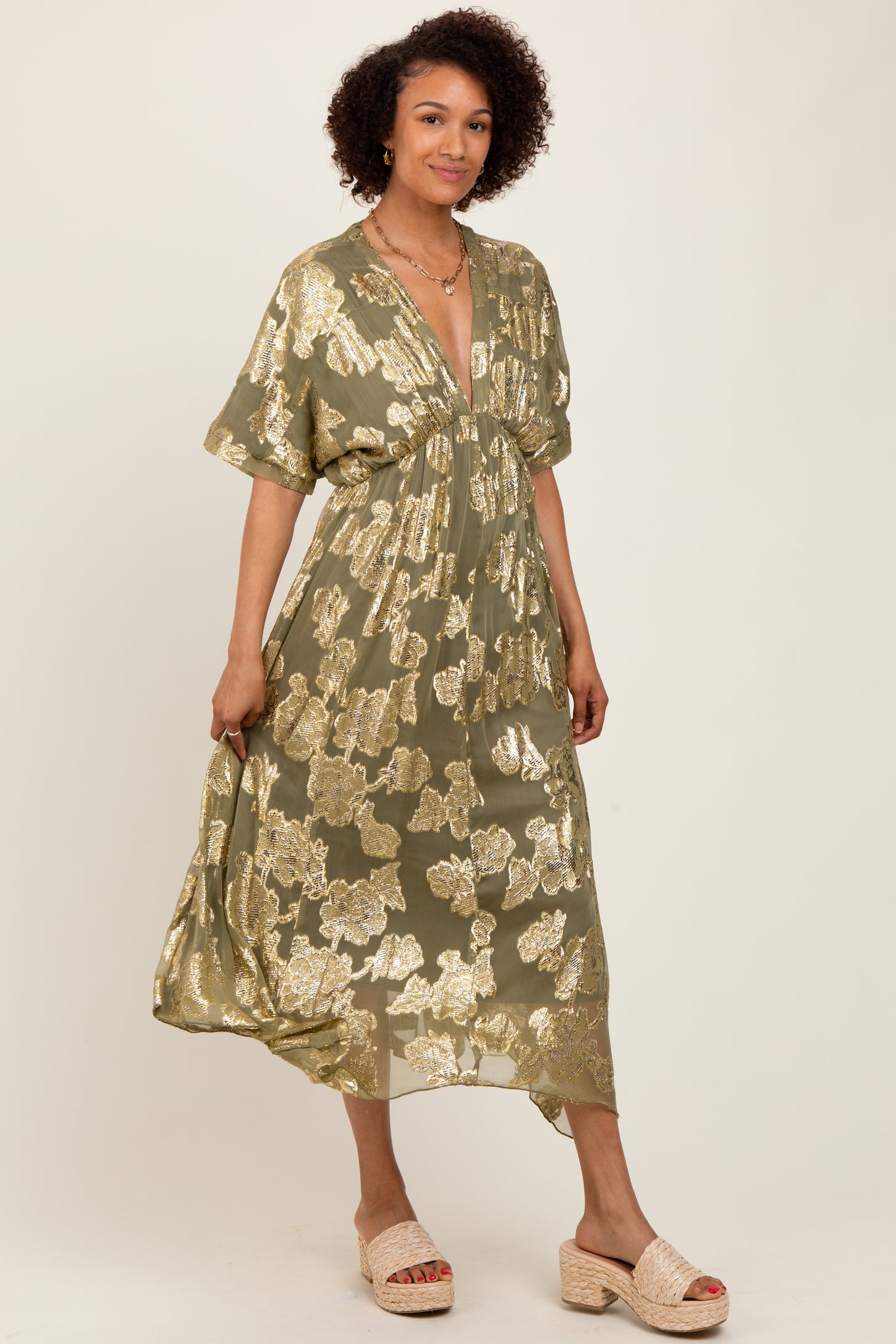 woman wearing an olive green floral maxi dress with metallic gold accents and a deep v-neckline
