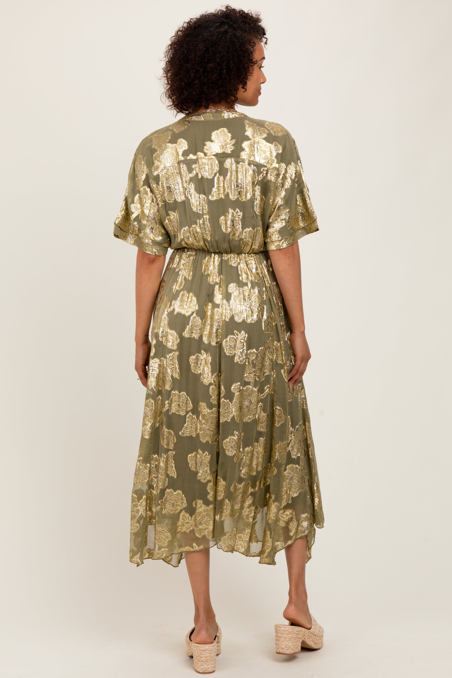 woman wearing an olive green maxi dress with gold floral print and a tie waist, viewed from the back
