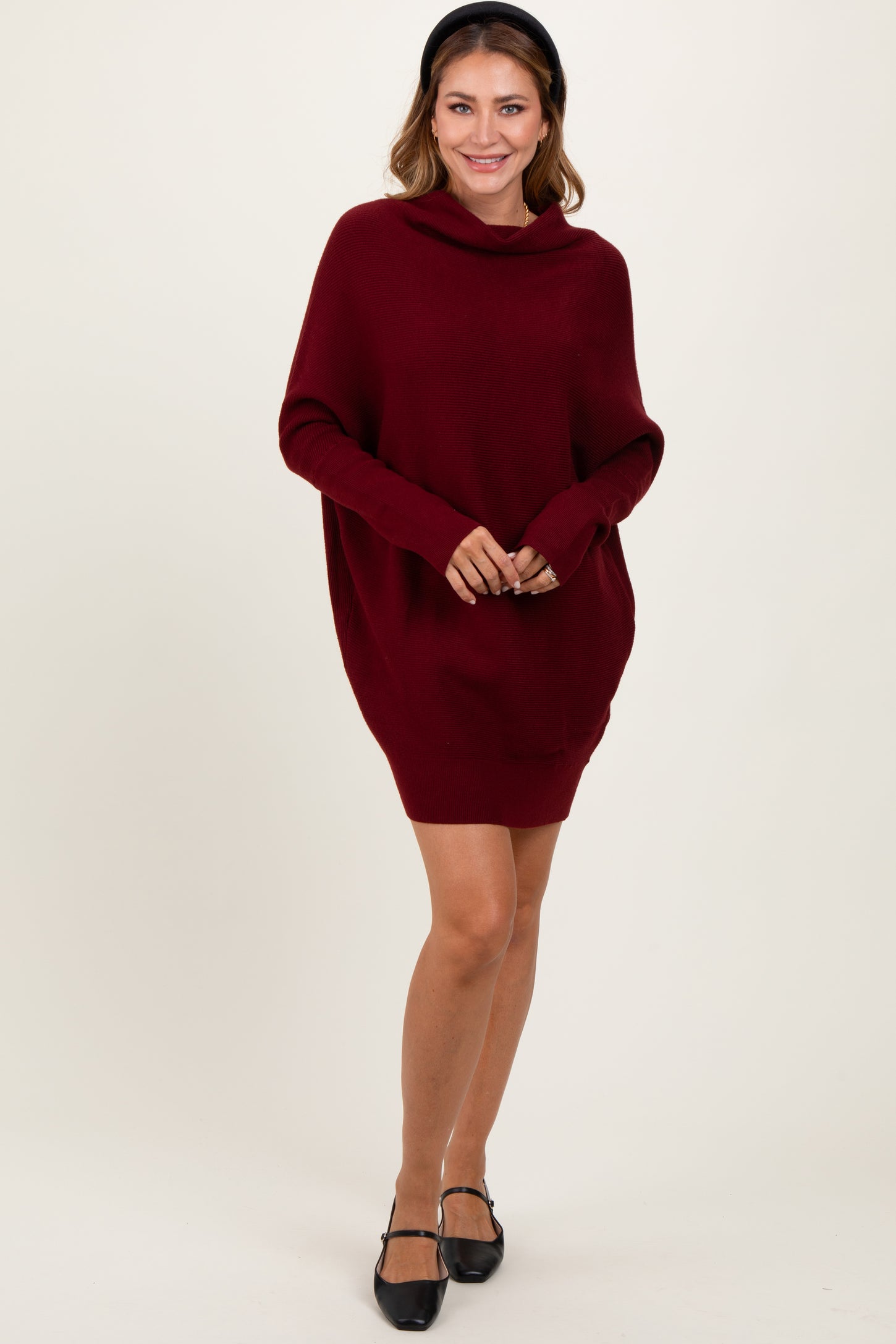 woman wearing a burgundy oversized sweater dress with a cowl neckline and long sleeves, smiling while standing