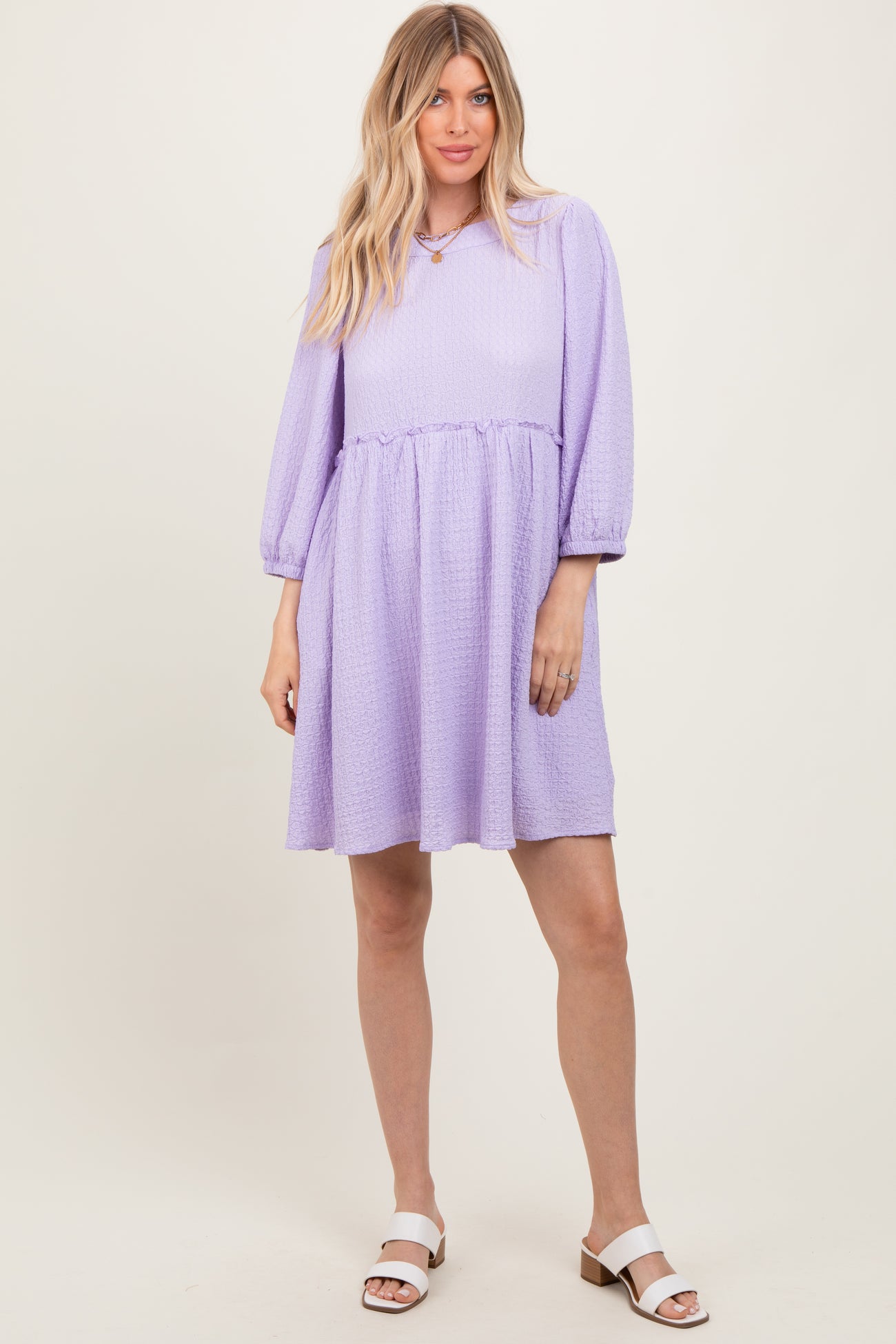 woman wearing a lilac puff sleeve dress with a smocked waist and a flared skirt, standing on a neutral background