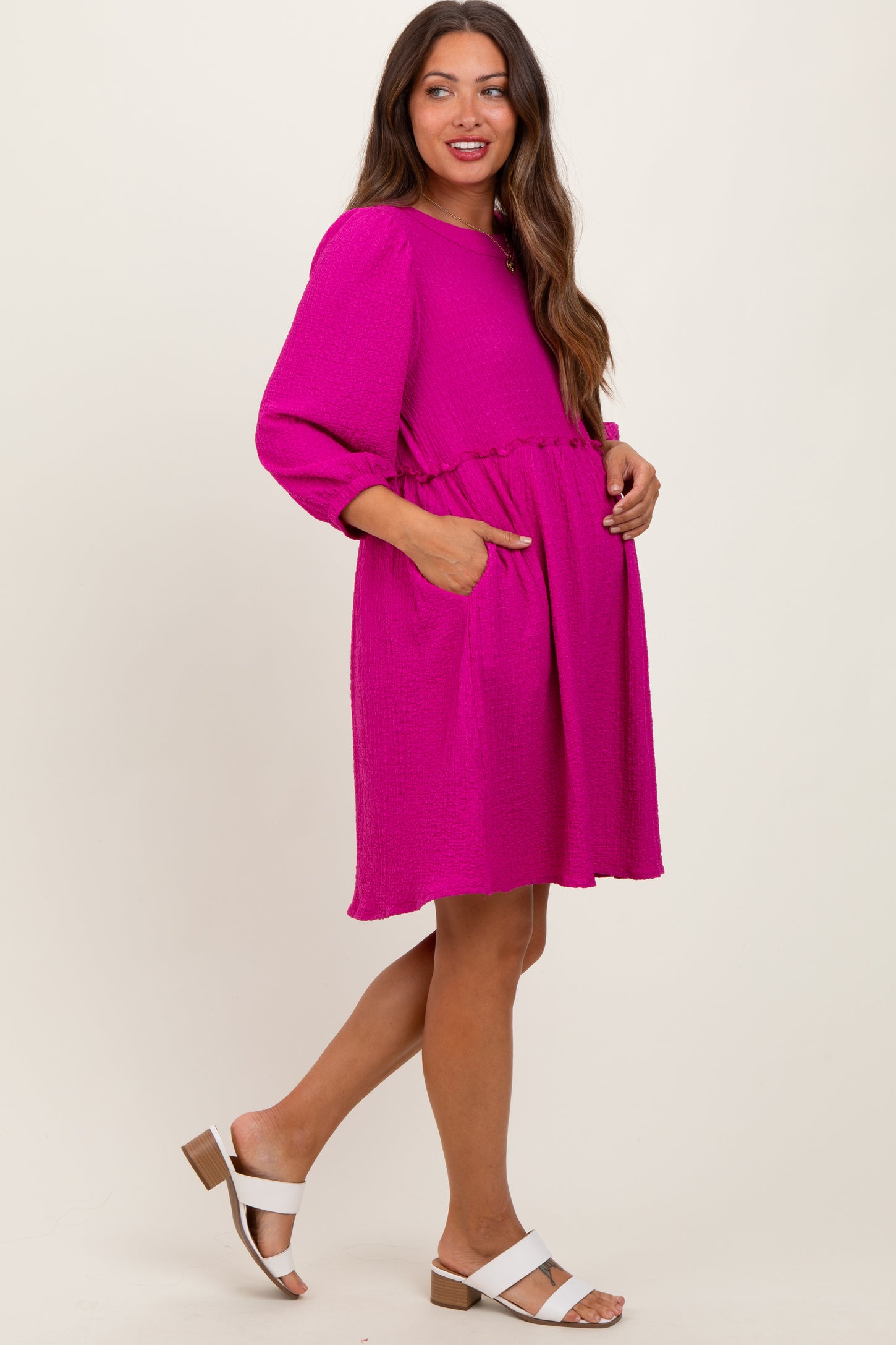 woman wearing a fuchsia maternity dress with a cinched waist and pockets, showcasing her baby bump while smiling