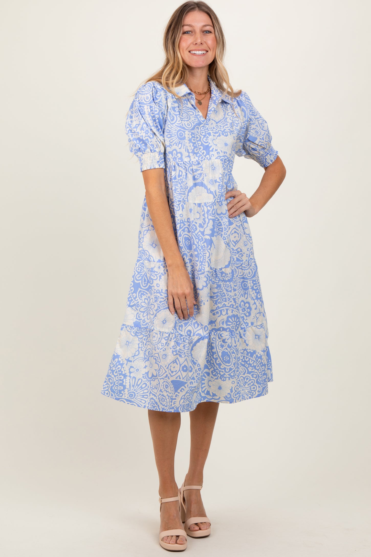 woman wearing a light blue floral midi dress with puff sleeves and a collar, standing and smiling