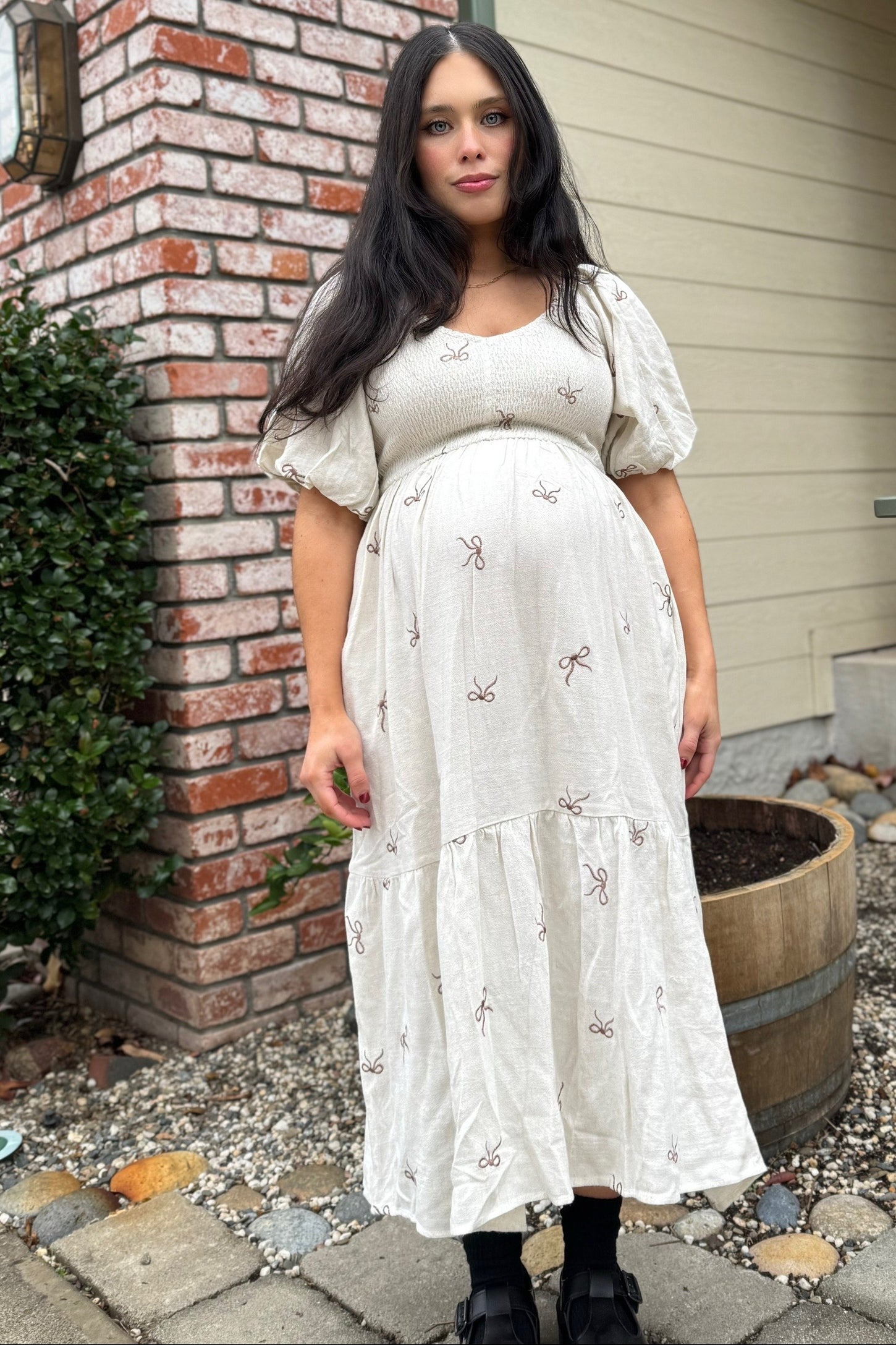 woman wearing a cream maternity dress with short puff sleeves and bow detailing, showing her baby bump