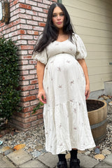 woman wearing a cream maternity dress with short puff sleeves and bow detailing, showing her baby bump